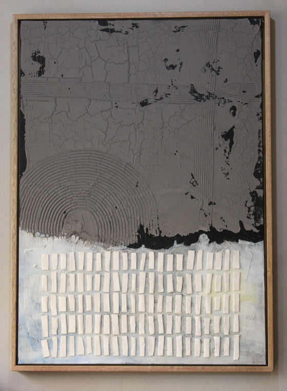 This mixed-media artwork contrasts a rugged, cracked upper half in deep charcoal gray with a lighter, textured lower half in soft whites and pale blues. A quiet resilience—blending raw materiality with delicate balance.