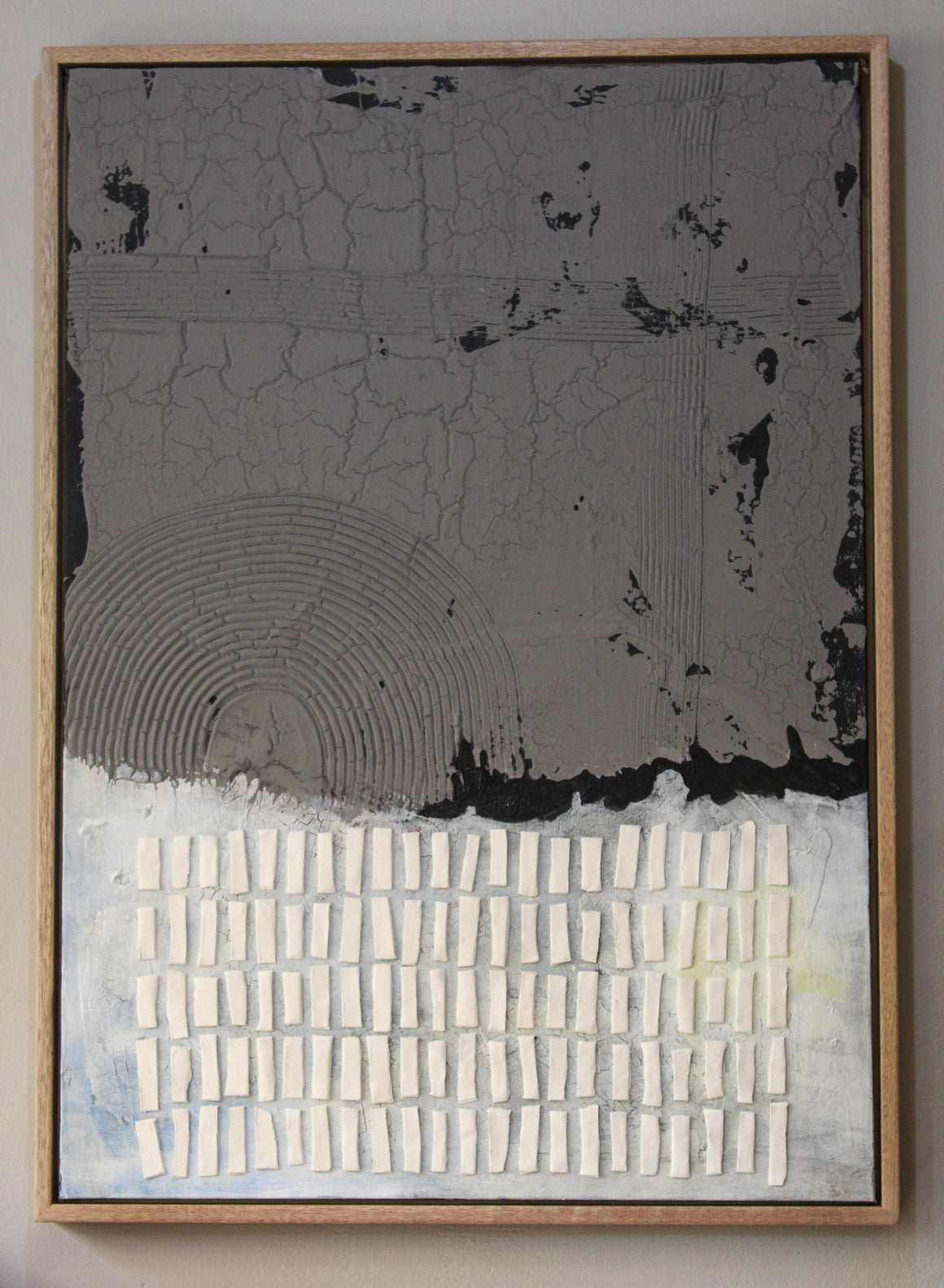 This mixed-media artwork contrasts a rugged, cracked upper half in deep charcoal gray with a lighter, textured lower half in soft whites and pale blues. A quiet resilience—blending raw materiality with delicate balance.