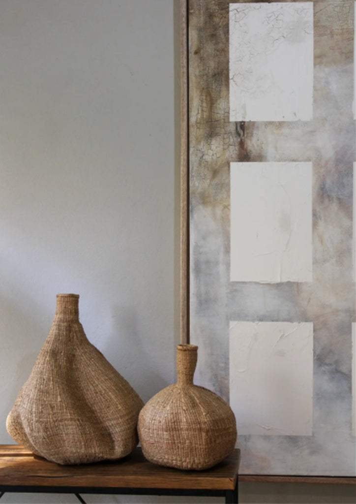 Two woven vases on a wooden surface with a textured wall in the background