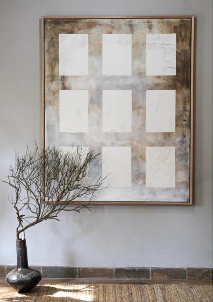 Framed abstract art piece on a wall with a vase and branches below.