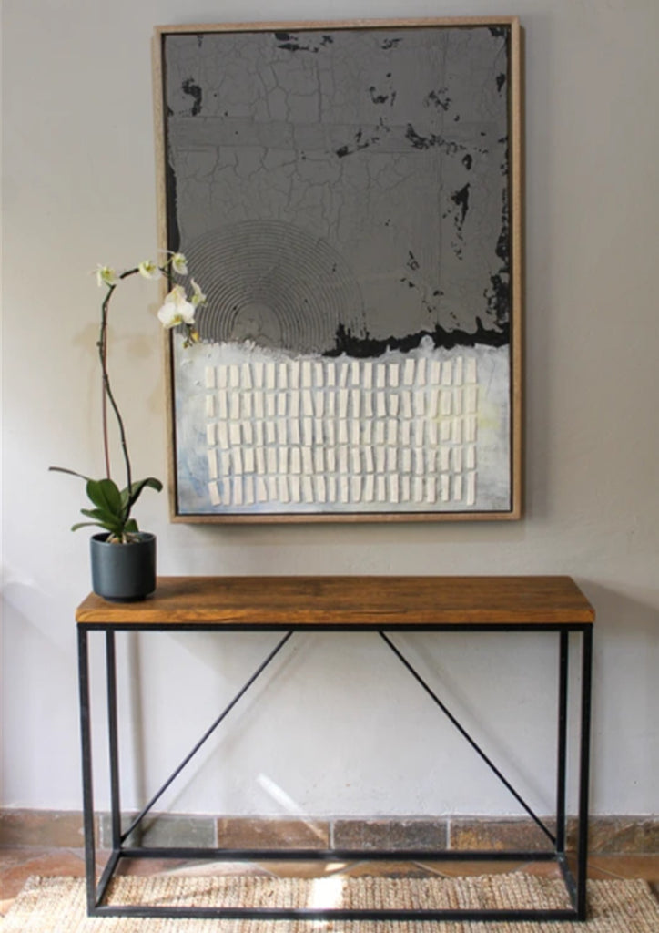 Wooden console table with a potted plant and abstract painting on a wall.